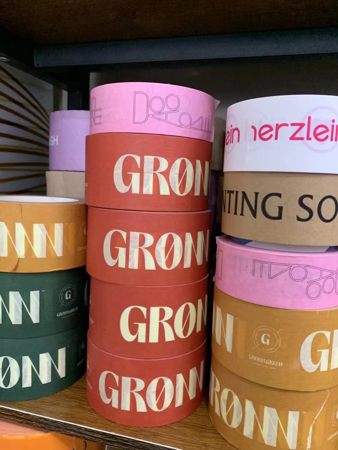 Stacked custom printed packing tape rolls in pink, red, green and brown with contrasting logos